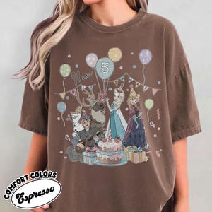 Puede incluir: Camiseta color espresso con un gr&aacute;fico colorido de personajes de dibujos animados, una tarta de cumplea&ntilde;os, globos y el n&uacute;mero 5. La palabra "Name" tambi&eacute;n es visible. La camiseta tiene un corte holgado.