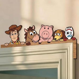 Può includere: Una decorazione in legno per porta raffigurante cinque personaggi dei cartoni animati di Toy Story: Woody, Bullseye, Hamm, Slinky Dog e Forky. I personaggi sono ritratti fino alla vita, con le mani appoggiate su un bordo orizzontale in legno.