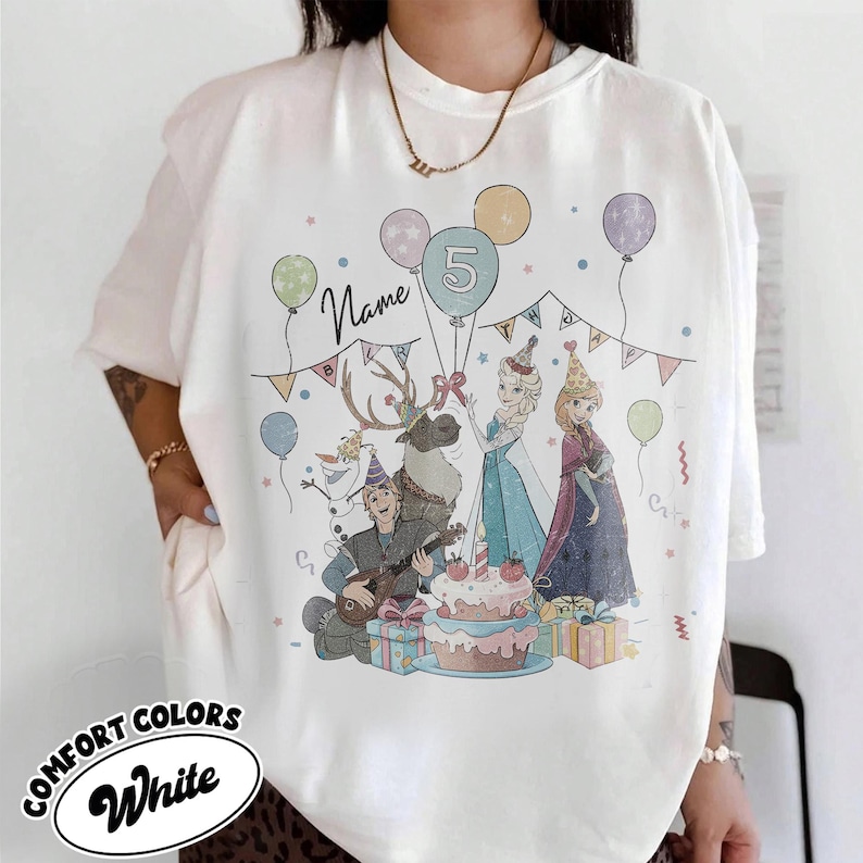 Puede incluir: Camiseta blanca Comfort Colors con un dise&ntilde;o de cumplea&ntilde;os colorido. El dise&ntilde;o incluye personajes de dibujos animados, globos, una tarta y el n&uacute;mero 5. La palabra "Name" tambi&eacute;n es visible en la camiseta.
