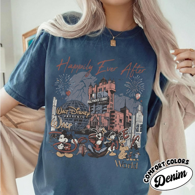Puede incluir: Camiseta azul marino con un gr&aacute;fico que presenta personajes de Disney y el texto "Happily Ever After". El dise&ntilde;o incluye el Hollywood Tower Hotel, fuegos artificiales y las palabras "Walt Disney World". La camiseta tambi&eacute;n tiene las palabras "Comfort Colors Denim".