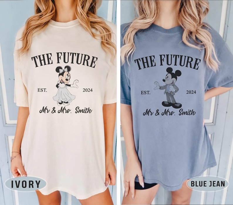 Puede incluir: Dos camisetas con un gr&aacute;fico de Mickey Mouse y Minnie Mouse. El texto en las camisetas dice "The Future Est. 2024 Mr & Mrs. Smith". Una camiseta es de color marfil y la otra es de color azul jean.