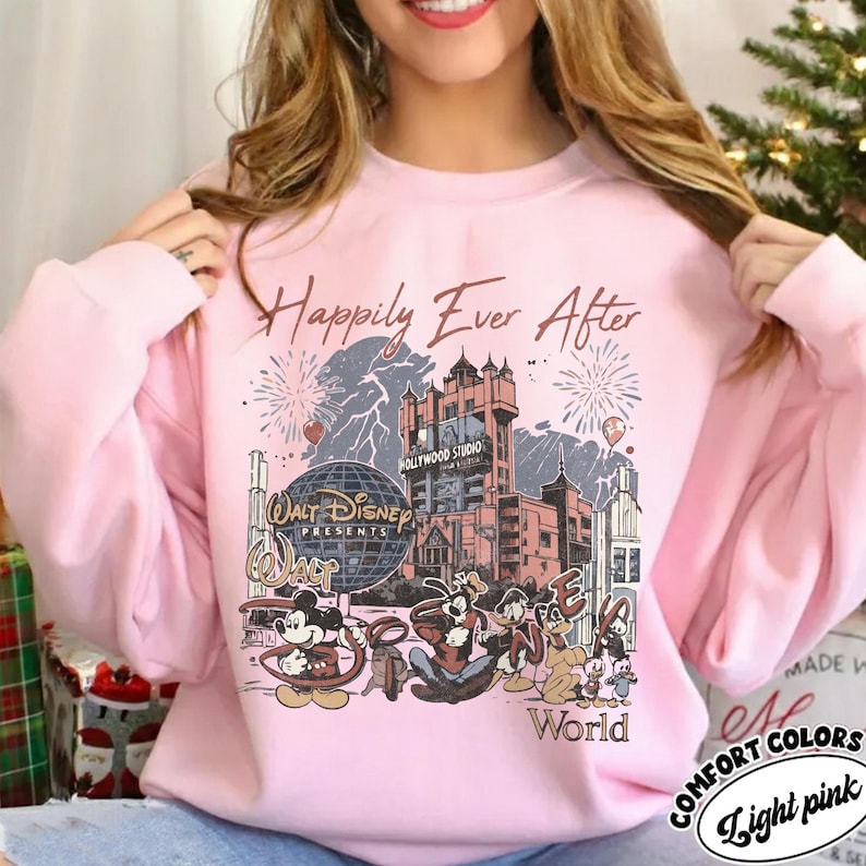 Puede incluir: Sudadera rosa claro con un dise&ntilde;o de Disney. El dise&ntilde;o incluye a Mickey Mouse, Goofy, Donald Duck y otros personajes, junto con el Hollywood Tower Hotel. El texto dice "Happily Ever After."