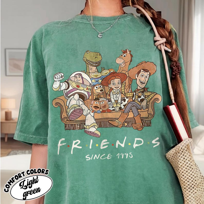 May include: Light green t-shirt featuring a graphic of characters from the movie Toy Story, seated on a couch. The word "FRIENDS" is printed below the graphic, with "SINCE 1995" underneath. The shirt also has the words "COMFORT COLORS" and "Light green" printed on it.