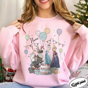 Puede incluir: Sudadera rosa claro con un gr&aacute;fico colorido de personajes de dibujos animados, globos y una tarta de cumplea&ntilde;os. El n&uacute;mero 5 se muestra en un globo. La palabra "Name" tambi&eacute;n se muestra en la sudadera.