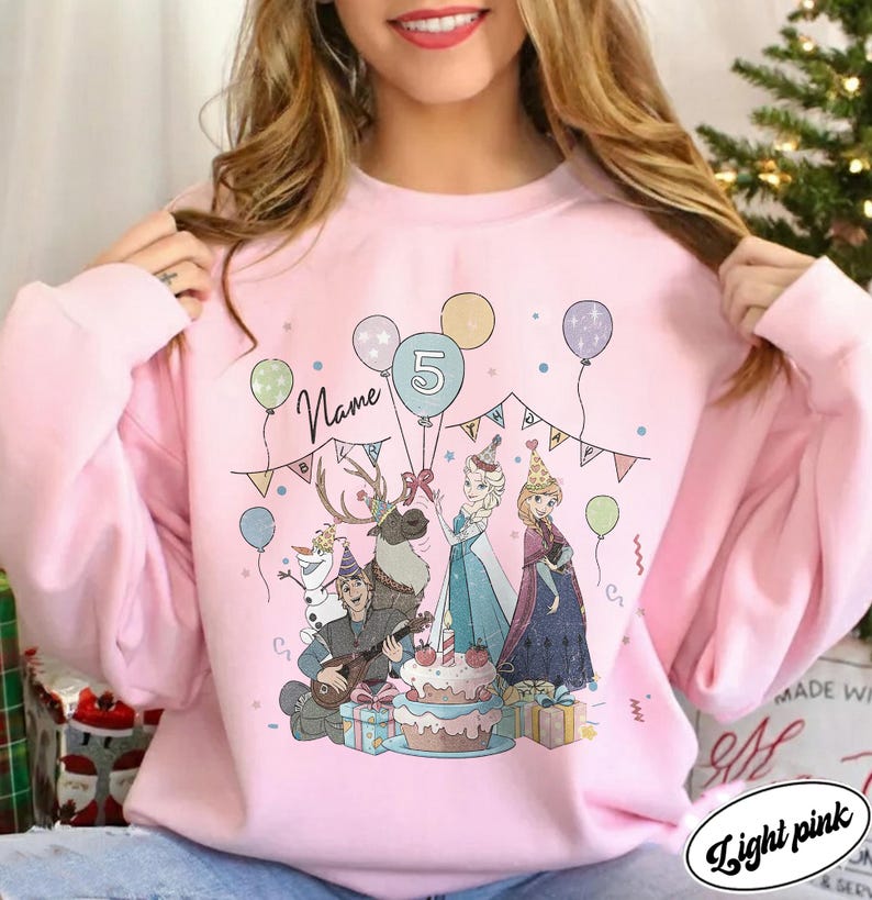 Puede incluir: Sudadera rosa claro con un gr&aacute;fico colorido de personajes de dibujos animados, globos y una tarta de cumplea&ntilde;os. El n&uacute;mero 5 se muestra en un globo. La palabra "Name" tambi&eacute;n se muestra en la sudadera.
