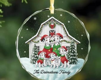 Peut inclure: Une décoration de Noël ronde en verre à facettes illustrant une grange blanche avec cinq chiens dalmatiens portant des pulls rouges et verts. Le texte "The Dalmatians Family" est inscrit en bas. Un ruban jaune est fixé au sommet.