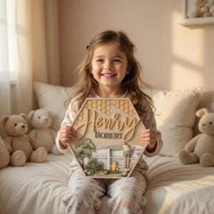 May include: A hexagonal wooden wall plaque featuring a layered design with the name Henry Robert in raised script and block lettering. The artwork depicts a scene with a fence, trees, and a yellow bear character, topped with a honeycomb pattern.