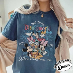 May include: A navy blue t-shirt featuring a colorful graphic of Disney characters, including Mickey and Minnie Mouse, Donald and Daisy Duck, and Goofy. The text "Walt Disney's Disneyworld" is above the characters, with "est. 1971" and "Where dreams come true" below.