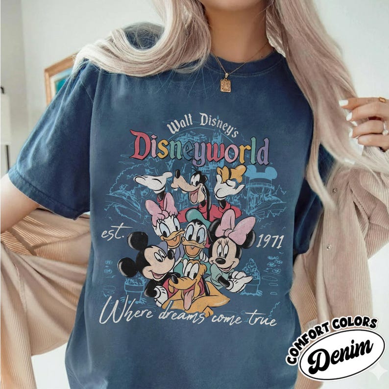 May include: A navy blue t-shirt featuring a colorful graphic of Disney characters, including Mickey and Minnie Mouse, Donald and Daisy Duck, and Goofy. The text "Walt Disney's Disneyworld" is above the characters, with "est. 1971" and "Where dreams come true" below.