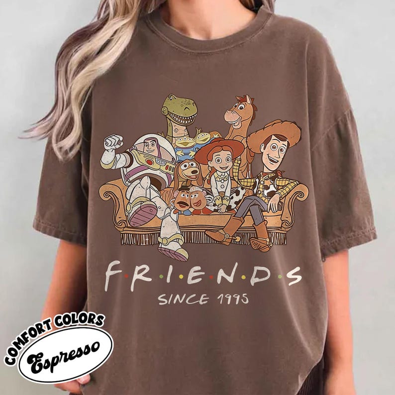May include: Espresso-colored t-shirt featuring a graphic of characters from the animated movie Toy Story. The word "FRIENDS" is printed in a colorful font, with "SINCE 1995" below. The shirt also has the words "COMFORT COLORS" and "Espresso" printed on it.