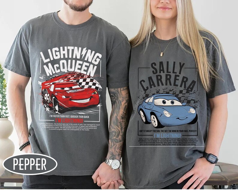 May include: Two gray t-shirts featuring characters from the movie Cars. One shirt displays Lightning McQueen with text, and the other features Sally Carrera with text. Both shirts have a vintage, distressed look.