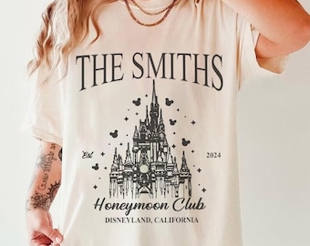 May include: A white t-shirt with a black graphic print of a castle with the text "The Smiths Honeymoon Club Disneyland, California" and the text "Est. 2024".