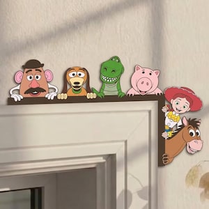 Puede incluir: Un marco decorativo de esquina con personajes de dibujos animados, incluyendo una figura de patata, un perro marrón, un dinosaurio verde, un cerdo rosa, una vaquera y un caballo marrón. Los personajes están dispuestos en los bordes del marco.