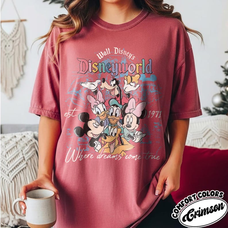 May include: Crimson Comfort Colors t-shirt featuring a Disney World graphic with Mickey Mouse, Minnie Mouse, Donald Duck, Daisy Duck, Goofy, and Pluto. The shirt has the text "Where dreams come true" and "est. 1971".