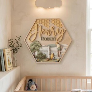 May include: A hexagonal wooden wall sign featuring a layered design with the names Henry and Robert in raised lettering. The artwork depicts a scene with a fence, trees, and characters, topped with a honeycomb pattern in light wood tones.
