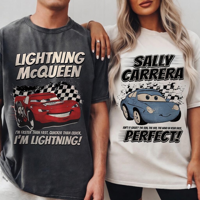 May include: Two t-shirts featuring characters from the movie Cars. One is dark gray with "LIGHTNING McQUEEN" and a red race car graphic. The other is white with "SALLY CARRERA" and a blue car graphic. Both shirts have text.