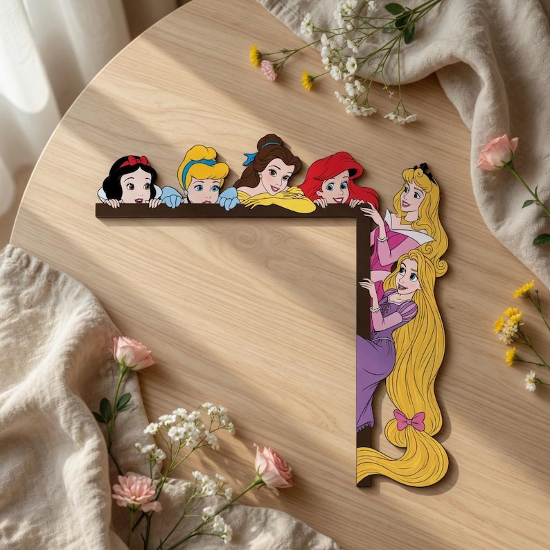 May include: An L-shaped wooden wall decor piece featuring six illustrated female characters. The top horizontal bar shows Snow White, Cinderella, Belle, and Ariel. The vertical bar shows Aurora and Rapunzel with long blonde hair.