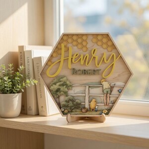 May include: A hexagonal wooden sign featuring a layered design with a honeycomb pattern at the top. The name Henry is written in large yellow script above the name ROBERT in green block letters. Below, a scene depicts a child and a bear.