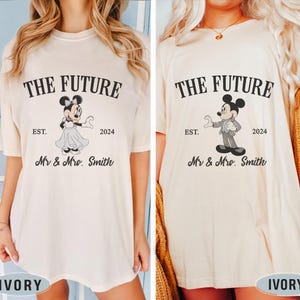 Puede incluir: Dos camisetas de color marfil con un estampado gr&aacute;fico de Mickey y Minnie Mouse. El texto en las camisetas dice "The Future" con el a&ntilde;o "2024" y "Mr & Mrs. Smith".
