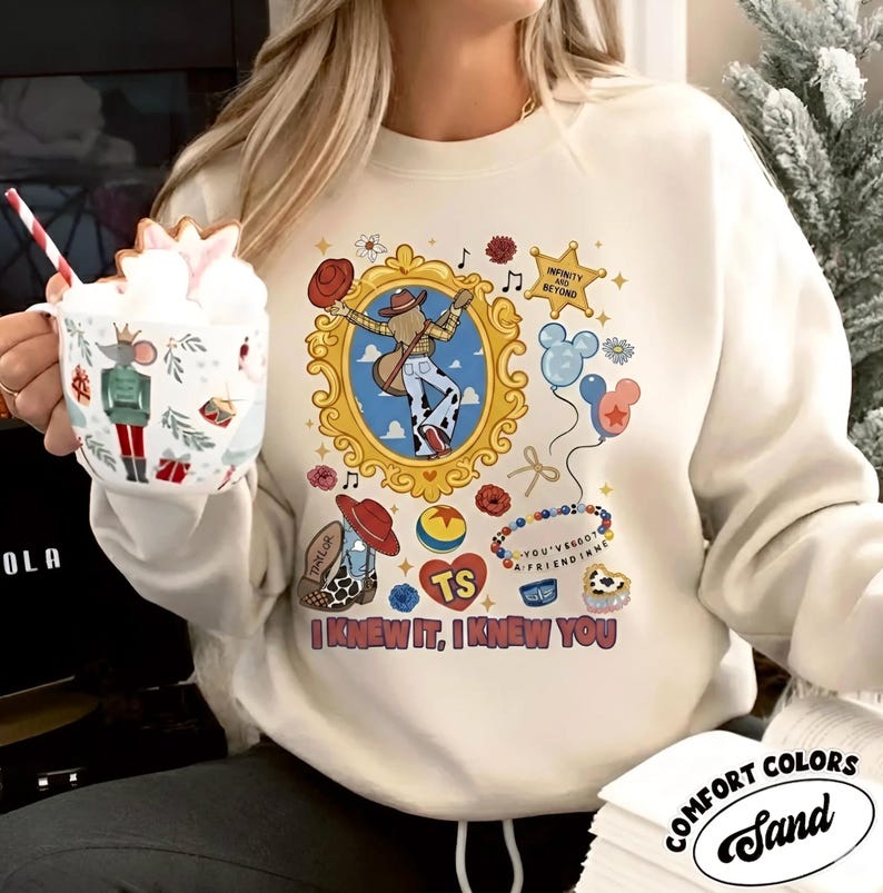 Puede incluir: Una sudadera de cuello redondo color crema con un estampado gr&aacute;fico de una persona con sombrero de vaquero y botas dentro de un marco dorado, rodeada de iconos como globos, una estrella con texto y la frase I KNEW IT, I KNEW YOU.