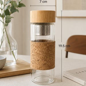 Könnte beinhalten: Eine transparente Glas-Tee-Infusionsflasche mit Bambusdeckel, Edelstahl-Infuser und Korkhülle. Die Flasche ist 7 cm breit und 19,5 cm hoch und hat ein Fassungsvermögen von 400 ml.