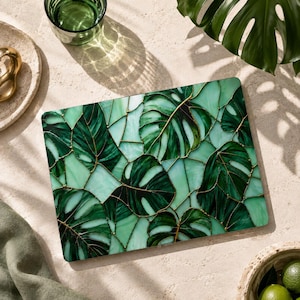 May include: A rectangular laptop skin featuring a stained glass style pattern of dark and light green monstera leaves. The design consists of various shades of green glass segments separated by thin gold lines, creating a mosaic effect.