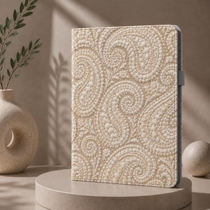 May include: A rectangular tablet case featuring a textured, cream-colored surface with an intricate, raised paisley pattern in white. The case has a slim profile, a grey side edge, and a small grey elastic loop attached to the right side for a stylus.