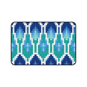 Op de afbeelding: Een rechthoekige mat met een herhalend geometrisch patroon van in elkaar grijpende ruitvormen. Het ontwerp bestaat uit een raster van kleine vierkantjes in tinten donkerblauw, middenblauw, lichtblauw, taling en wit, wat een symmetrisch motief vormt.