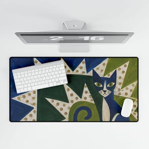 May include: A rectangular desk mat featuring a stylised blue cat illustration against a background of green and blue geometric shapes with gold polka dots. A white wireless keyboard and a white computer mouse are placed on the mat surface.