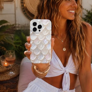 Op de afbeelding: Een smartphonehoesje met een wit iriserend schubpatroon dat lijkt op parelmoer. Het hoesje heeft een uitsparing voor een camera met drie lenzen en is afgewerkt met een gladde, glanzende laag die het licht op een subtiele wijze weerkaatst.