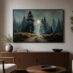 Può includere: Una stampa artistica da parete rettangolare che raffigura un paesaggio boschivo scuro e suggestivo di notte. Un sentiero sterrato conduce attraverso alti pini in silhouette verso una luna piena luminosa al centro di un cielo nebbioso blu e grigio.