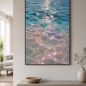 May include: A rectangular wall art print featuring a high-angle view of ocean water with gentle ripples. The surface displays a gradient of deep blue transitioning into turquoise and soft pink hues, with bright sunlight reflecting off the water.