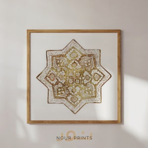 Puede incluir: Una impresión enmarcada de una estrella de ocho puntas dorada y blanca con intrincadas caligrafías y diseños florales. La estrella está sobre un fondo blanco.