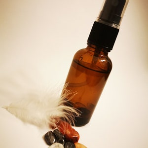 May include: A brown glass bottle with a black spray top filled with a clear liquid. The bottle is surrounded by a white feather and several small, colourful stones.