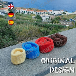 May include: Four handmade crochet baskets in yellow, blue, red, and brown. The baskets are cylindrical with a textured appearance. The image also includes the text "ORIGINAL DESIGN".