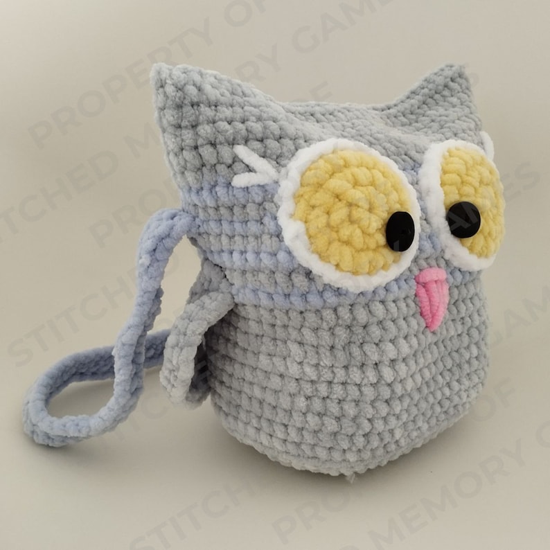 May include: A gray crocheted owl-shaped bag with a light blue strap. The owl has yellow and white eyes and a pink tongue.