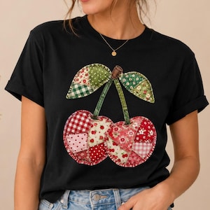 Peut inclure: T-shirt noir avec un motif de cerises en patchwork. Les cerises sont faites de tissu à motifs rouges, roses et blancs, avec des feuilles vertes et une tige marron. Le t-shirt a des manches courtes et un col rond.