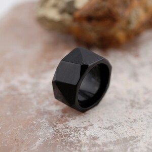May include: A black geometric ring with a faceted design. The ring is made of a smooth, polished material.