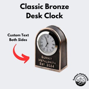 May include: A classic bronze desk clock with a white face and black hands. The clock has a custom text area on both sides. The text on the front reads "SUMMIT METALSMITH EST. 2024".
