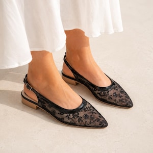 Könnte beinhalten: Schwarze Slingback-Flats aus Spitze mit spitzer Zehenpartie und kleinem Absatz. Die Flats haben ein florales Spitzenmuster und eine Paspel aus Lackleder. Der Slingback-Riemen hat einen kleinen Schnallenverschluss.