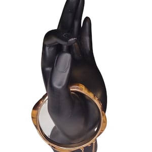 May include: A circular bangle bracelet featuring a brown and tan striped pattern with a smooth, polished finish. The bracelet is constructed with a gold-toned metal frame and includes a small, delicate gold-toned safety chain attached to the side.