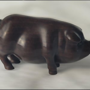 May include: A dark brown wooden pig figurine. The pig is standing on all four legs and has a slightly curved back. The pig's snout is pointed and its ears are small.