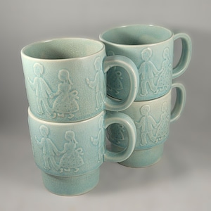 May include: Four light blue ceramic mugs with a raised design of couples dancing. The mugs are stacked on top of each other.