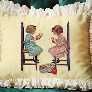 May include: A decorative pillow with a cream-colored ruffled border. The center features a vintage illustration of two young girls seated on chairs, knitting with red yarn. The background is a soft yellow, and the pillow has a square shape.