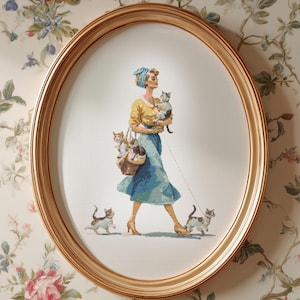 May include: An oval framed cross-stitch shows a woman in a yellow top and blue skirt, carrying cats and walking two cats on leads. The artwork is set against floral wallpaper, with a gold-coloured frame.