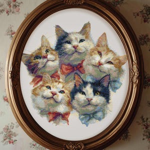 Könnte beinhalten: Ein oval gerahmtes Kunstwerk mit einer Gruppe von fünf Katzen mit verschiedenen Fellfarben, darunter orange, grau und schwarz-weiß. Jede Katze trägt eine Fliege in Rot- und Blautönen. Der Rahmen ist goldfarben.