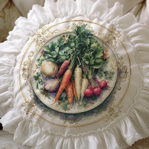 Op de afbeelding: Rond wit kussen met een gerimpelde rand. Het midden toont een gedetailleerde illustratie van verschillende groenten, waaronder wortelen, radijsjes en uien, gerangschikt op een decoratief bord. Het kussen heeft een kanten rand.