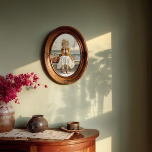 May include: An oval framed print of a young girl in a dress, seated with a basket. The frame is a warm brown color, and the print is mounted on a light green wall. A bouquet of pink flowers in a ceramic vase sits on a wooden table.