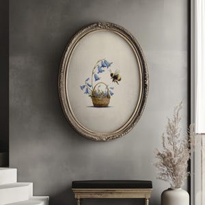 May include: An oval framed print depicts a basket of bluebell flowers with a bee. The artwork is in a vintage style, with a detailed illustration of the flowers and bee. The frame is ornate with a gold finish, adding to the classic aesthetic.