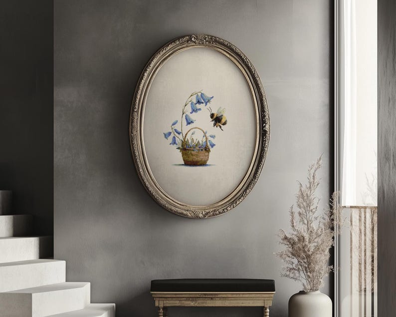 May include: An oval framed print depicts a basket of bluebell flowers with a bee. The artwork is in a vintage style, with a detailed illustration of the flowers and bee. The frame is ornate with a gold finish, adding to the classic aesthetic.